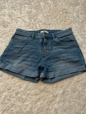 Blå jeansshorts med uppvik - Klassiska blå jeansshorts med uppvikta benslut och femficksmodell. Perfekta för varma dagar och enkla att matcha med allt. Stängs med dragkedja och knapp framtill.