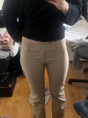 Low waist kostymbyxor med knappar - Snygga beiga kostymbyxor  med bootcut-modell och dubbla knappar i midjan. Dessa är knappt använda och i mycket bra skick! 