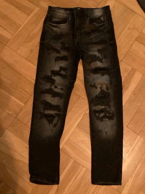 Jordan Craig Legency edition svarta jeans med slitning enligt design storlek 12 år - Säljer ett par Jordan Craig svarta jeans med designade slitningar framtill. Jeansen har fem fickor, smal passform och en cool, tvättad look. Perfekta för dig som gillar en edgy och trendig stil. Storlek junior 12 år.