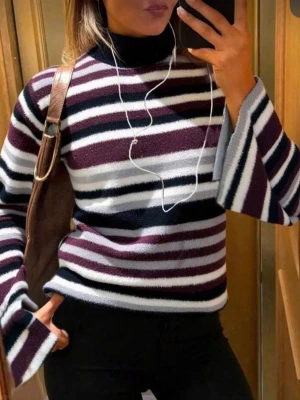 Randig polotröja med vida ärmar - Stickad polotröja med breda ränder i vinrött, svart, vitt och grått. Tröjan har vida ärmar och hög polokrage. Mjuk och skön kvalitet, perfekt för kyligare dagar. Passar till både jeans och kjol för en trendig look.