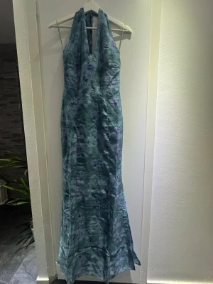 Blommig långklänning från Adoore - Supersnygg långklänning från Adoore i blå och gröna toner med blommigt mönster. Klänningen har halterneck och en smickrande passform som framhäver figuren. Perfekt för dig som vill sticka ut med en elegant look.