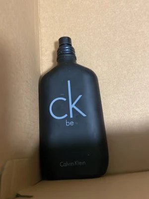 CK Be parfym från Calvin Klein 1/4 full - Minimalistisk parfymflaska i matt svart glas från Calvin Klein med texten 'ck be' i vitt på framsidan. Flaskan har en stilren och modern design som känns både klassisk och ungdomlig.