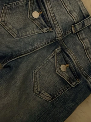 Blå jeans med fickdetaljer - Säljer ett par blå jeans med snygga ficklock och silverfärgade knappar. Jeansen har en tvättad look och är utsvängda. Har lite fläckar men inget som syns ❤️ 279 men säljer för 95