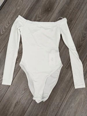 Vit off-shoulder body Stradivarius - Snygg vit body från Stradivarius med off-shoulder design och långa ärmar. Tillverkad i stretchigt material som sitter tight och bekvämt. Perfekt att styla med jeans eller kjol för en trendig look.