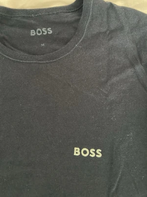 Svart BOSS t-shirt i bomull - Snygg svart t-shirt från BOSS med diskret logga broderad på bröstet. Klassisk rund halsringning och korta ärmar. Tillverkad i mjuk bomull som känns skön mot huden. Perfekt till jeans eller shorts för en clean och enkel stil.