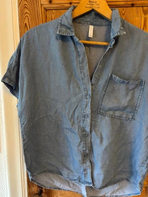 Blå kortärmad skjorta i bomull - Snygg blå skjorta i mjuk bomull med korta ärmar och klassisk krage. Skjortan har knappar framtill och en bröstficka för en avslappnad look. Perfekt till jeans eller shorts för en chill stil.