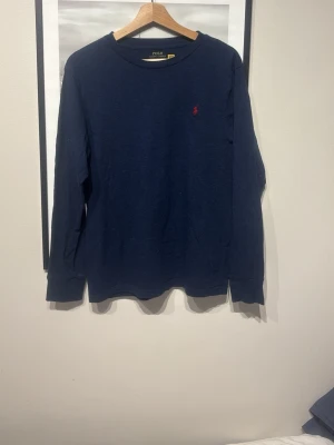 Mörkblå långärmad tröja Polo Ralph Lauren - Mörkblå långärmad tröja från Polo Ralph Lauren med klassisk röd broderad logga på bröstet. Tröjan har rund halsringning och ribbade muddar vid ärmslut och nederkant. Perfekt för en stilren och enkel look. Pris kan diskuteras använd ca 4 gånger 