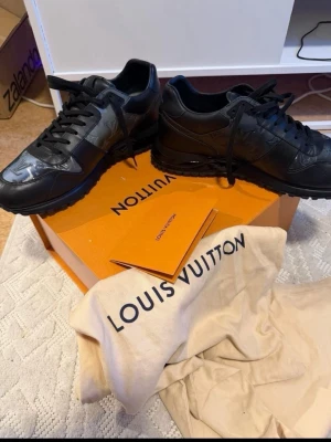 Svarta Louis Vuitton sneakers - Snygga svarta sneakers från Louis Vuitton med diskreta logodetaljer och svarta skosnören. Skorna har en låg silhuett och är tillverk fta i läder och textil. Perfekta för dig som vill ha en exklusiv och stilren soppa till vardagslooken.