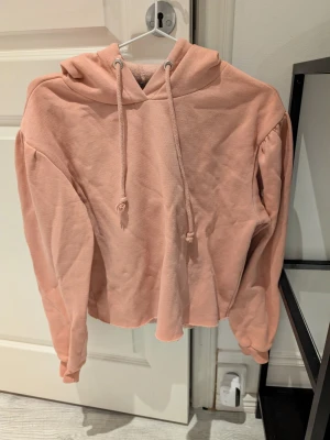 Ljusrosa croppad hoodie med puffärm - Säljer en ljusrosa croppad hoodie med puffärmar och huva med dragsko. Hoodien har en avslappnad passform och är gjord i mjukt sweatshirtmaterial, perfekt för en chill och trendig look. Xs/s