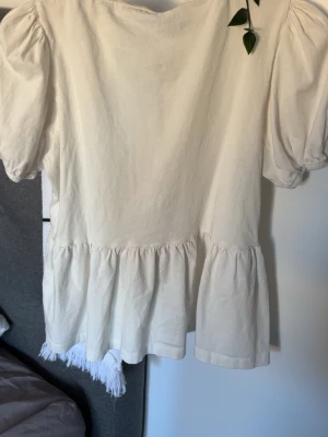 Beige blus med puffärm och knyt - Supersöt beige blus med puffärmar och volang nertill. Baksidan har tre dekorativa knytband som ger en unik look. Tillverkad i mjuk bomull, perfekt för dig som gillar romantisk och avslappnad stil.