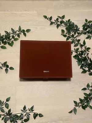 DAY ET Jewelry Box Big – Nutmeg/Rostbrun • Ny med lapp - DAY ET Jewelry Box Big i färgen Nutmeg (rostbrun/terrakotta) – helt nytt med originallapp! 🌿 Mjukt sammetsmaterial med DAY ET-logga i guld. Massor av fack för ringar, örhängen, armband & halsband + stort spegel i locket. 📐 25×18×12 cm | Tryckknappsrem ✔ Nytt med lapp – oanvänt! ⚠️ Mindre märken på baksidan, syns ej vid användning. Nypris: ~699 kr | Style No: 3225490902​​​​​​​​​​​​​​​​