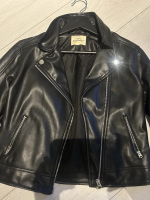 Svart skinnjacka från KappAhl - Snygg svart skinnjacka från KappAhl med klassisk bikerstil. Jackan har silvriga dragkedjor, bred krage och två fickor framtill. Perfekt för dig som vill ha en tidlös och cool look. Köptt den begagnat och vet inte vilken storlek den är i för dem har klippt bort de men skulle säga xs-s, skriv för mer frågor!💕