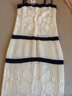 Stickad virkad klänning XS svart/vit - Supersöt stickad virkad klänning från Gina Tricot  i krämvitt med svarta detaljer. Klänningen har smala axelband, blommigt mönster och är kort i modellen. Perfekt för sommarens alla tillfällen och ger en trendig, bohemisk vibe.