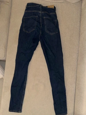 Mörkblå skinny jeans med hög midja - Säljer ett par mörkblå skinny jeans med hög midja och klassiska fem fickor. Jeansen har smal passform och är tillverkade i stretchigt denimtyg för en bekväm känsla. Perfekta till en avslappnad stil.