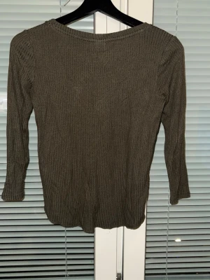 Olivgrön ribbstickad tröja - Snygg olivgrön ribbstickad tröja med rund halsringning och långa ärmar. Tröjan har en smal passform och är tillverkad i ett mjukt, stretchigt material som sitter skönt på kroppen. Perfekt att matcha med jeans eller kjol.