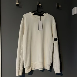 Vit sweatshirt från C.P. Company - Säljer en stilren vit sweatshirt från C.P. Company. Den är i använt skick. Perfekt för både vardag och chill. Passar bra till jeans eller joggers!