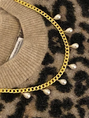 Guldhalsband med droppformade pärlor - Snyggt halsband i guldtonad metall med droppformade vita pärlor som hängande detaljer. Kedjan har en chunky design som ger ett trendigt intryck och pärlorna ger en elegant touch. Perfekt accessoar för att lyfta vilken outfit som helst.