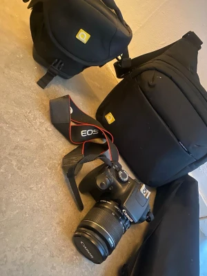 Canon EOS digitalkamera med väska - Säljer en svart Canon EOS digitalkamera med tillhörande objektiv och kamerarem. Ett till objektiv Medföljer två svarta vadderade kameraväskor och ett stativ 160 cm typ . Kameran har klassisk design och tydliga reglage, perfekt för dig som vill ta snygga bilder.