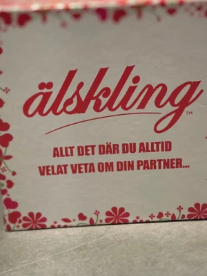 Sällskapsspel Älskling - Roligt sällskapsspel med titeln 'Älskling', perfekt för par som vill lära känna varandra bättre. Spelet har en vit och röd design med blommönster och texten 'Allt det där du alltid velat veta om din partner...'.