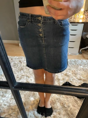 Mörkblå jeanskjol med knappar - Snygg mörkblå jeanskjol med flera silverfärgade knappar framtill och klassiska fickor. Kjolen har en kort längd och små slitsar i sidorna för extra stil. Perfekt att matcha med en crop top eller hoodie. Ej bra pris,,,skriv til mig. Knappt använd