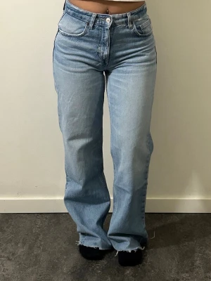 Ljusblå raka jeans med rå kant - Snygga ljusblå jeans med rak passform och mid-rise . Jeansen har klassiska fem fickor och rå, fransad kant nertill för en trendig look. 