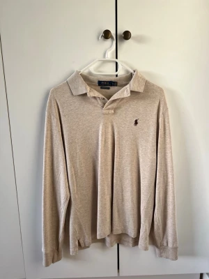 Ralph Lauren långärmad piké - strl M - Beige långärmad pikétröja från Polo Ralph Lauren i storlek M med krage och knappar framtill. Tröjan har broderad logga på bröstet och är gjord i mjuk bomull. 