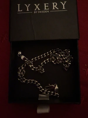 Silverfärgat kedjehalsband Lyxery - Snyggt silverfärgat halsband från Lyxery by Sweden. Halsbandet har en klassisk, lite tjockare kedja med blanka länkar som ger en stilren och modern look. Perfekt accessoar för att lyfta din outfit och matcha med andra smycken.