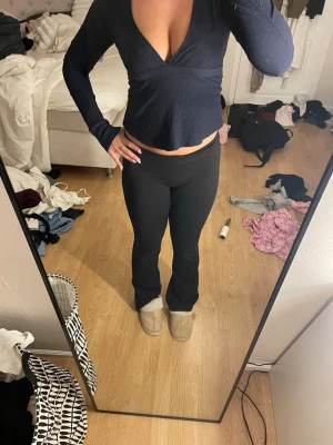 Mörkblå omlottopp med långa ärmar - Snygg mörkblå omlottopp med långa ärmar och djup v-ringning. Toppen har en knytning i ryggen och är tillverkad i ett stretchigt, ribbat material. Perfekt för dig som gillar en trendig och figurnära stil. Har en fläck på armen som inte går bort 