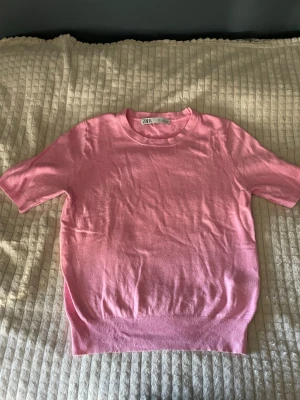 Rosa kortärmad tröja från Zara - Snygg rosa tröja från Zara med korta ärmar och rund halsringning. Tröjan är i ett mjukt, tunt stickat material och har ribbade muddar vid ärmslut och nederkant. Perfekt för en trendig och avslappnad look.(Tröjan är lite nopprig men är något som går att få bort med en noppbortagare)