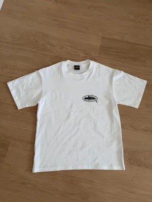 Vit t-shirt med tryck från Corteiz - Vit t-shirt från Alcatraz med svart tryck av fängelset på bröstet. Klassisk rund halsringning och korta ärmar. Tillverkad i mjuk bomull som känns skön mot huden. Perfekt för dig som gillar enkel och stilren design. Corteiz!