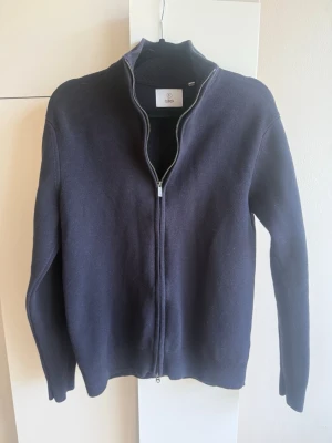 Mörkblå ziptröja från Filippa K - Stilren mörkblå ziptröja från bläck. Tröjan är ribbstickad vid ärmslut och nederkant, perfekt för lager-på-lager. Enkel och klassisk design som passar till det mesta.