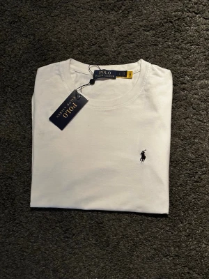 Vit t-shirt från Polo Ralph Lauren - Storlek L passar snarare S/M .Vit t-shirt från Polo Ralph Lauren med klassisk rund hals och den ikoniska broderade loggan på bröstet. Enkel och stilren design som passar till allt. Tillverkad i mjuk bomull för skön känsla hela dagen.