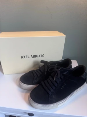 Axel Arigato Clean 90 Suede svart - Snygga svarta sneakers från Axel Arigato i modellen Clean 90 Suede. Skorna är gjorda i mocka med klassisk låg siluett, svarta skosnören och vit sula. Perfekta för dig som gillar minimalistisk och stilren design.