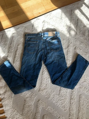 Ralphl lauren jeans - Säljer ett par klassiska blå jeans i slim fit-modell med raka ben och fem fickor. Jeansen har en snygg tvätt och detaljer som bälteshällor och knappgylf. Perfekta för en avslappnad och trendig stil.