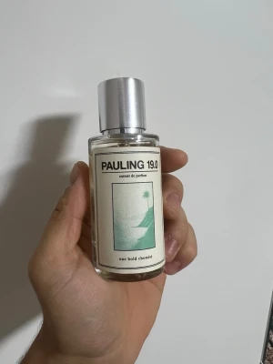 Pauling 19.0 Extrait de Parfum - Pauling 19.0 Extrait de Parfum från One Bold Chemist. Flaskan är genomskinlig med en silverfärgad spraykork och minimalistisk etikett i vitt och grönt med en palmillustration. Modern och stilren design som passar perfekt i badrumshyllan.
