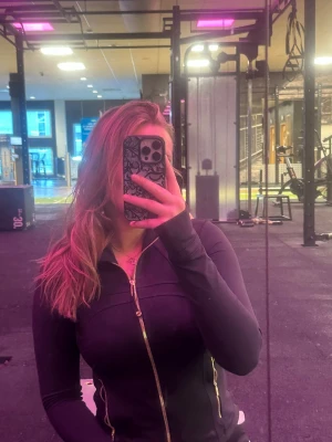 Svart träningsjacka med dragkedja - Snygg svart träningsjacka med hel dragkedja framtill och figurnära passform. Jackan har långa ärmar och diskreta sömdetaljer som ger en sportig look. Perfekt för gymmet eller löprundan.  Storlek 6, den kortare modellen
