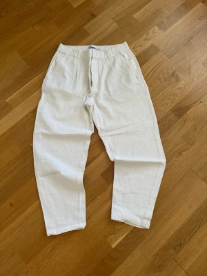 Vita linnebyxor från Zara - Snygga vita linnebyxor från Zara med rak passform och texturerat tyg. Byxorna har hällor för skärp, knapp och dragkedja framtill. Perfekta för en avslappnad och trendig stil.