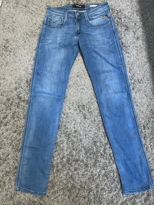 Replay Anbass - Snygga blå jeans från Replay med klassisk femficksdesign och ljus tvätt. Jeansen har dragkedjegylf, tydliga sömmar och en läderpatch med logga bak i midjan. Perfekta för dig som gillar en smal passform och stilren look.