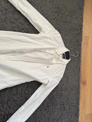 Vit skjorta från Ralph Lauren - Klassisk vit skjorta från Ralph Lauren med custom fit och den ikoniska broderade loggan på bröstet. Skjortan har långa ärmar, knappar framtill och är tillverkad i mjuk bomull. Perfekt för en clean och stilren look.