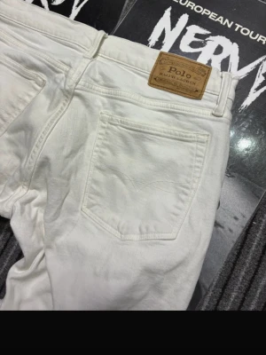 Vita jeans från Polo Ralph Lauren - Snygga vita jeans från Polo Ralph Lauren med klassisk femficksdesign och läderpatch bak i midjan. Jeansen har raka ben och är tillverkade i ett mjukt bomullstyg som känns bekvämt hela dagen. Perfekta för en clean och fräsch look. OBSS- finns ett par fläckar på framsidan, backsidan, och vid bälte ringen. Skriv om de är ngt 🤩