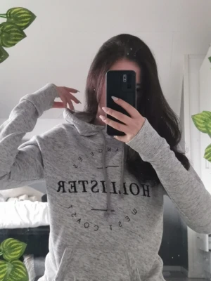 Grå Hollister hoodie med tryck - Snygg grå hoodie från Hollister med svart tryck framtill där det står 'Hollister West Coast' och 'Los Angeles'. På ryggen står det 'California'. Hoodien har dragsko i huvan och är i mjukt material, perfekt för en chill look.