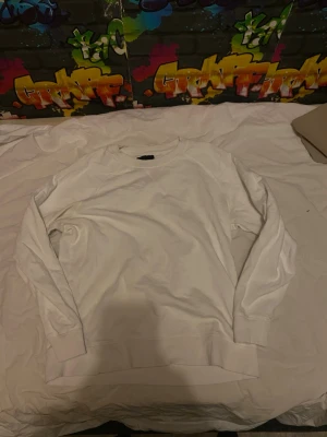 Vit crewneck sweatshirt - En stilren vit crewneck sweatshirt med långa ärmar och ribbade muddar vid ärmslut och nederkant. Perfekt för en clean och avslappnad look. Materialet ser ut att vara mjukt och bekvämt, troligen bomull eller bomullsblandning. Behöves dock strykning.