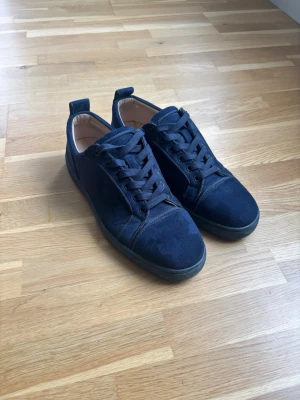 Mörkblå louboutin skor - Snygga mörkblå  louboutin sneakers i mocka med klassisk låg profil och mörkblå snören. Skorna har en stilren design med diskreta sömmar och röd sula. Perfekta för dig som gillar en clean och enkel look. Insidan är ljusbeige för extra kontrast. Och väl omhändertagna använda någon enstaka gång 