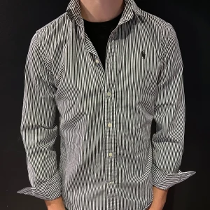 Randig skjorta från Ralph Lauren - Säljer en klassisk svartvit randig skjorta från Ralph Lauren med broderad logga på bröstet. Skjortan har lång ärm, knappar framtill och krage. Perfekt för dig som gillar stilrena plagg med snygg passform.