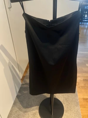 Svart midikjol  - En stilren svart kjol med rak passform. Kjolen har en enkel och elegant design utan synliga detaljer eller mönster, vilket gör den lätt att styla.
