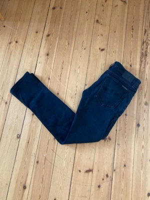 Mörkblå jeans från Nudie Jeans - Säljer ett par mörkblå jeans från Nudie Jeans med klassisk femficksmodell och smal passform. Jeansen har diskreta sömmar på bakfickan och en svart patch i midjan. Perfekta för dig som gillar stilrena och tidlösa jeans.
