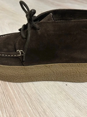 Bruna mockaloafers från Gant - Snygga loafers från Gant i mörkbrun mocka med beige detaljer och grov gummisula. Skorna har klassisk snörning framtill och en kontrasterande läderdetalj baktill med Gant-logga. Perfekta för en stilren och avslappnad look.