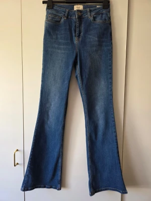 Blå bootcut jeans från Pulz modell Livia - Snygga blå bootcut jeans från Pulz med klassisk femficksdesign och normal midja. Jeansen har utsvängda ben och är gjorda i mjukt denimtyg som ger en skön passform. Perfekta för en trendig och avslappnad stil.