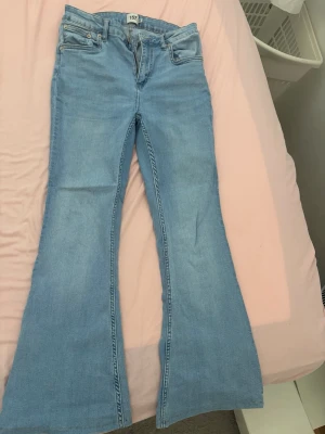 Ljusblå utsvängda jeans 157 L - Säljer ett par ljusblå jeans från 157 i storlek L med kort längd. Jeansen har utsvängda ben och klassisk femficksmodell. Perfekta för dig som gillar retrovibbar och vill ha ett par bekväma och snygga jeans till din garderob.