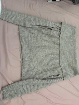Ljusgrå ribbstickad off shoulder-tröja - Trendig ljusgrå ribbstickad tröja med bred off shoulder-krage. Mjuk och stretchig kvalitet som sitter snyggt på kroppen. Perfekt till jeans eller kjol för en avslappnad men stilsäker look. Långa ärmar och croppad passform.